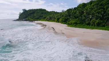 Hava aracı 4K alçak irtifa uçuşu tropikal kumlu plajın üzerinde Mahe Adası, Seyşeller 'de okyanus dalgaları ile uçar.