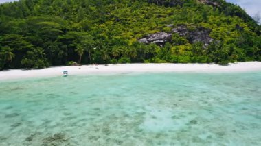 Mükemmel beyaz kumlu tropik cennet kumsalı, turkuaz lagün suyu, ıssız bir tekne ve sahildeki bir çiftin hava aracı görüntüsü. Yaz tatili kavramı