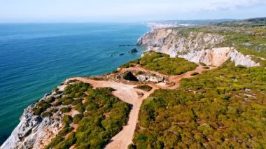 Praia da Adraga plajının 4K Aerial düzenli görüntüleri. Beyaz Atlantik Okyanusu dalgaları turistlerle kumsala doğru yuvarlanıyor. Sintra, Portekiz