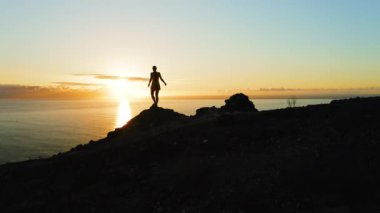 Kadın silueti gün batımında elleri havada dağa tırmanıyor. Gece, okyanusun derinliklerinde yalnız bir kızla birlikte. Los Gigantes Tenerife 'nin hava manzarası.