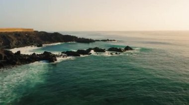 Güçlü okyanus dalgaları zümrüt sularına çarpar. Güçlü akıntılar girdap gibi süzülür ve siyah volkanik kayalara çarpar. Büyüleyici hava aracı görüntüsü.