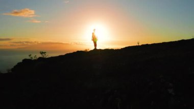 Gün batımında kız silueti. Turuncu gökyüzüne karşı dağın tepesi. Güneş doğuyor ve parlıyor..