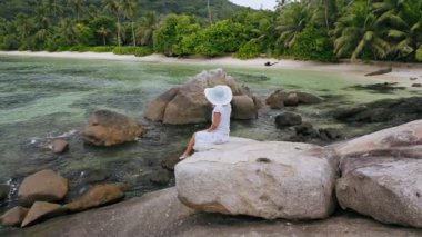 Seyşeller 'in egzotik doğasıyla çevrili granit kayanın üzerinde oturan sarışın kızın hava dairesi görüntüleri. Yaşam tarzı, seyahat ve eğlence konsepti