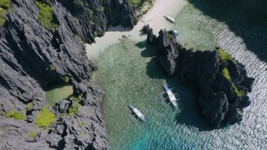 4K Havacılık, Filipinler, El Nido, Miniloc adasındaki Gizli Göl Sahili 'ndeki engebeli karst kayalıkları arasında demirlemiş turist teknelerinin daire aşağı 4K görüntüleri.