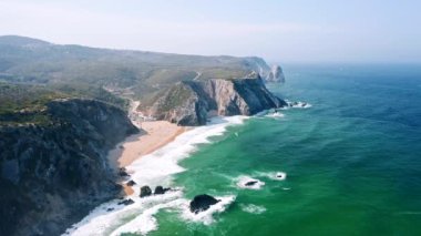 Atlantik Okyanusu 'nun 4K Havacılık manzarası. Portekiz Praia Grande plajı yakınlarındaki kayalık kayalıklara doğru beyaz dalgalar akıyor.