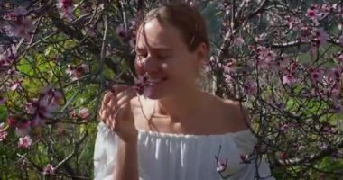 Bahar elma bahçesinde doğanın tadını çıkaran genç bir kadının doğal güzelliği. El kamerası görüntüleri. Çiçek açan ağaçlarıyla gülümseyen mutlu kız. Yavaş çekim yakın çekim.