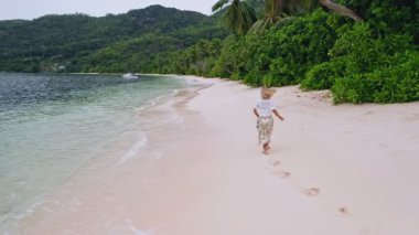 Seyşeller. İnsansız hava aracı, Mahe Adası 'ndaki palmiye ağaçlarıyla cennet sahilinde koşan genç bir kadını takip ediyor. Seyahat kavramı
