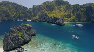 Filipinler, Palawan, El Nido 'daki Shimizu ve Miniloc Adası arasındaki boğazın 4K hava görüntüsü. Turist tekneleri turnede. Güzel mavi su manzarası ve kireçtaşı dağları var..