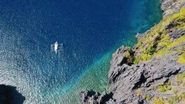 Güneşli bir günde açık denizde turkuaz ve berrak suyla hareket eden teknenin havadan aşağı görüntüsü. Tekne tropikal gölden ayrıldı. El Nido, Palawan Adası, Filipinler.