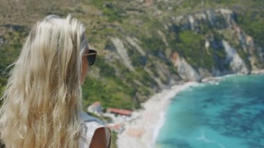 Güneş gözlüklü sarışın kadın deniz koyuna bakıyor manzaralı manzarayı kutluyor tatil macerasının tadını çıkarıyor doğa.