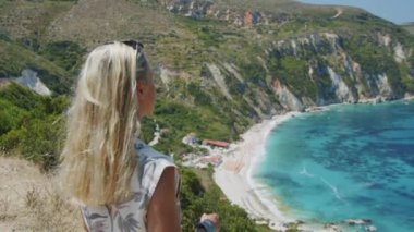 Dağın tepesinde gezen sarışın kadın güzel deniz koyuna bakıyor manzaralı manzarayı kutluyor tatil macerasının tadını çıkarıyor doğa