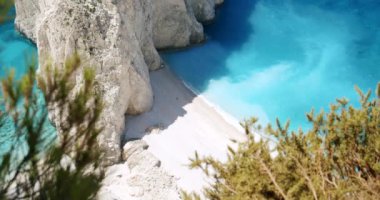 Mavi gölü olan büyük beyaz kayalık bir kumsal, turistik zevk tekneleri. Uçurumun tepesinden çam ağaçları görünüyor..