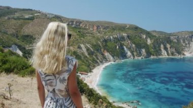 Dağın tepesinde gezen sarışın kadın güzel deniz koyuna bakıyor manzaralı manzarayı kutluyor tatil macerasının tadını çıkarıyor doğa