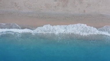 Kumlu sahil manzarası ve kıyı kenarındaki turkuaz deniz dalgaları. Yaz tatili sahnesi