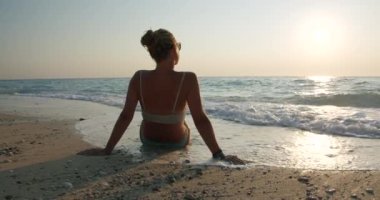 Altın gün batımında plajda dinlenen bir kadının yakınına. Dişi gezgin okyanus dalgalarının tadını çıkarıyor..