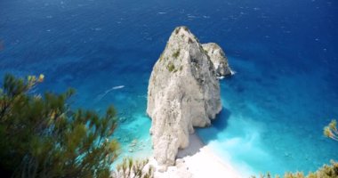 Mavi gölü olan büyük beyaz kayalık bir kumsal, turistik zevk tekneleri. Uçurumun tepesinden çam ağaçları görünüyor..