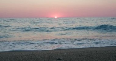 Romantik deniz batımı arka planı. Mor renkli gökyüzü bulutsuz ve dalgalı bir çakıl taşı kumsalına doğru.