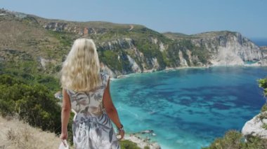 Dağın tepesinde gezen sarışın kadın güzel deniz koyuna bakıyor manzaralı manzarayı kutluyor tatil macerasının tadını çıkarıyor doğa.