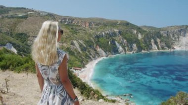 Dağın tepesinde gezen sarışın kadın güzel deniz koyuna bakıyor manzaralı manzarayı kutluyor tatil macerasının tadını çıkarıyor doğa.