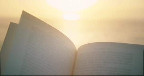 日没の空を背景に神聖なオープンブック 紙のページが点灯 古代の聖書に照らされたテキスト クルアーンを読む — ストック動画