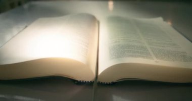 Yavaş çekimde açık bir kitabın parlak sayfaları. Bilgi kavramı okunuyor. Ev kütüphanesinde sinema ışığı. Kutsal yazılar Kutsal İncil.