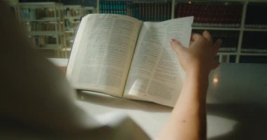 Kadın kütüphanede kitap okumayı kendi kendine öğrendi. Açık bir kağıdın kadın eli sayfasını çeviriyor. Eğitim kavramını öğreniyorum. Ağır çekimde yakın çekim.