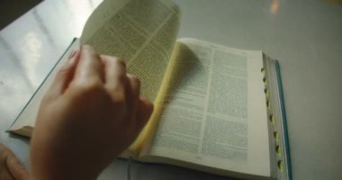 Kutsal İncil 'in sayfalarını kütüphanede beyaz masa üzerinde çeviriyor. Okuma kavramı, edebiyat alanında bilgi arayışı. Eğitim ve eğitim. Üst ve alt görünümü kapat.