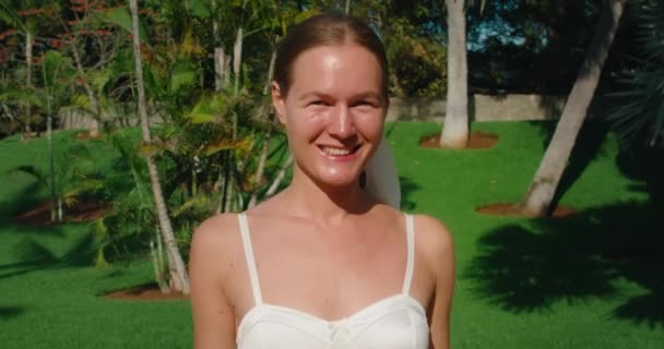 一个快乐快乐的女人带着棕榈树在热带花园散步的画像 风对着她的头发 摆出相机 健康的生活方式 特写慢动作 — 图库视频影像