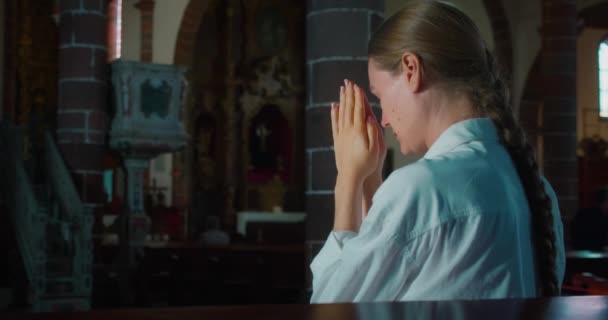 女性は暗い教会の一角で神への祈りの中で頭を下げました 贖い主キリストに祈りの手を折りました キリスト教の宗教的概念 — ストック動画