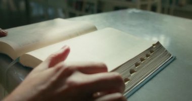 Kadın kütüphanede kitap okumayı kendi kendine öğrendi. Açık bir kağıdın kadın eli sayfasını çeviriyor. Eğitim kavramını öğreniyorum. Ağır çekimde yakın çekim.