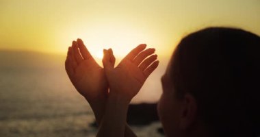 Kadın ellerinin iki eliyle uçan kuş güvercini silueti yaptığını yakından görebiliyoruz. Barış ve özgürlük kavramı. Okyanus sahili, parlak gün batımı ışığında..