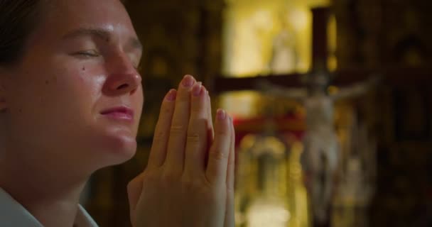 기독교 여성은 십자가에 그리스도의 배경에 대하여 교회에서 무릎을 기도합니다 클로즈업 — 비디오