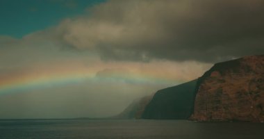 Ufukta gökkuşağı görünüyor. İspanya 'nın Tenerife Kanarya Adaları' ndaki volkanik kayalık sahilde. Los Gigantes uçurumları. Yağmurdan sonra güneşli hava.