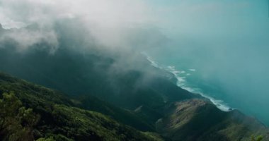 Kalın sis bulutları okyanus kıyısındaki dağ manzarasına doğru iniyor. Yukarıdan sinematik deniz manzarası.