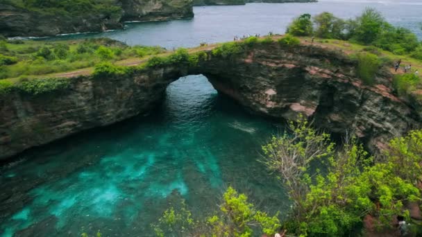 位于印度尼西亚巴厘岛努沙佩尼达岛上的破碎的海滩小湾 热带岩石海岸与自然桥拱 墙壁上自然洞的空中景观 — 图库视频影像