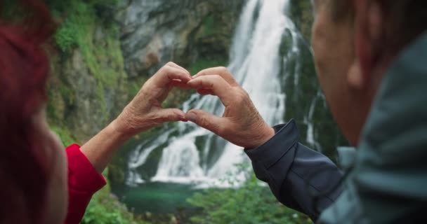 年上の引退したカップルは オーストリアの滝にハイキングしながら手でハートを作りました どんな年齢でも旅行するという愛の概念 ザルツブルクのゴリンジャー落下 — ストック動画