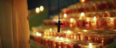 Dini haçı elinde tutan kişi kilisede yanan mumlar yakıyor. Tanrı 'ya Hristiyan inancı. Tanrı 'nın Tapınağı.