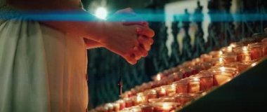 Kilisede yanan mumların yanında dua eden bir kadın. Yetişkin bir kız ellerini katlayarak günahlarının kefaretini ödedi. Doğal ateş ışığı arkaplanı.