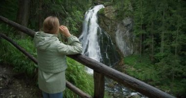 Avusturya dağlarında şelalenin tadını çıkaran bir kadın gezgin. Dağlarda seyahat, macera ve gezi konsepti. Kız ormandaki doğanın güzelliğini düşünüyor..