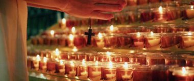 Kilisede yanan mumların yanında dua eden bir kadın. Yetişkin bir kız ellerini katlayarak günahlarının kefaretini ödedi. Doğal ateş ışığı arkaplanı.