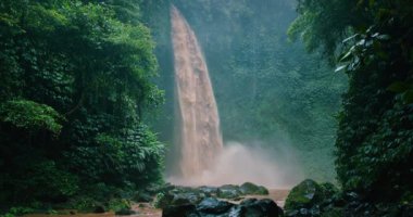 İnanılmaz Nungnung şelalesi deresi. Düşen su kayalara ve yemyeşil yapraklara çarpıyor. Bali Endonezya. Yakın çekim sinematik görünüm.