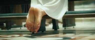 Uzun elbiseli çıplak ayaklı bir kadın kilisede diz çöküp dua ediyor. Ayaklara yakın çekim.