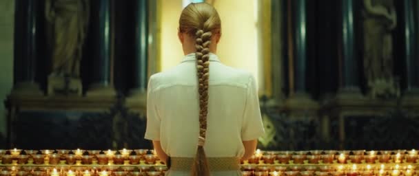 在教堂里 一个满头辫子的女人在点燃蜡烛前祈祷 她的背影映入眼帘 特写手持式电影胶片 — 图库视频影像