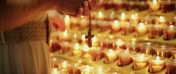 木の十字架と祈りを握っている女性の手 大聖堂で燃えるワックスキャンドル — ストック動画