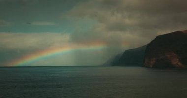 Ufukta gökkuşağı görünüyor. İspanya 'nın Tenerife Kanarya Adaları' ndaki volkanik kayalık sahilde. Los Gigantes uçurumları. Yağmurdan sonra güneşli hava.