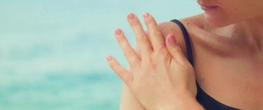 Kadın, deniz suyuyla kaplı bir plajda omuzlarına güneş kremi sürüyor. İnce dişinin okyanusa karşı yakın çekimi. Kızlar el kremini yavaş çekimde sürerler.