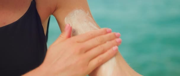 女性手部的特写用Spf乳霜涂在覆盖着摩尔的皮肤上 在有海水背景的海滩上 女孩在肩上涂防晒霜 — 图库视频影像