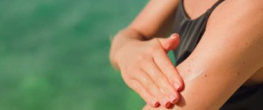 Genç bir kadının tatilde deniz kıyısındaki bir plajda cildine dikkat etmek için güneş kremi ya da güneş kremi sürmesine yakın çekim. Vücutta benlerle kaplı SPF kremi. Kız lekeleri