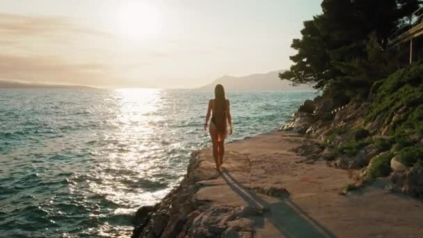 Seorang Wanita Berjalan Sepanjang Jalan Pantai Dengan Matahari Mencerminkan Dari — Stok Video