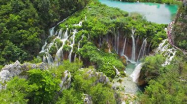 Hırvatistan 'daki Plitvice Gölleri Ulusal Parkı' nda insanlar dar yolda yürüyüş yapıyor. Bir sürü su ve şelalesi olan dağ manzarası. Seyahat ve doğa kavramı.